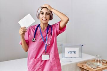 Sticker - Young nurse woman at political campaign election holding envelope stressed and frustrated with hand on head, surprised and angry face