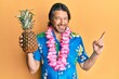 Middle age handsome man wearing hawaiian lei holding pineapple smiling happy pointing with hand and finger to the side