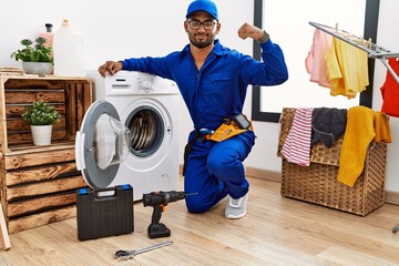 Poster - Young indian technician working on washing machine strong person showing arm muscle, confident and proud of power