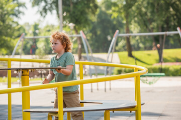 curly boy having fun on carousel in summer park.