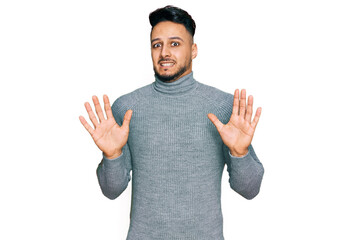 Young arab man wearing casual clothes afraid and terrified with fear expression stop gesture with hands, shouting in shock. panic concept.