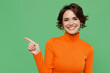 © ViDi Studio - Young smiling woman 20s in casual orange turtleneck point index finger aside on workspace area mock up isolated on plain pastel light green color background studio portrait. People lifestyle concept