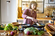 Young woman frying vegetables on cooking pan while cooking healthy food in the kitchen at home. Lots of fresh food ingredients on table. Modern kitchen interior