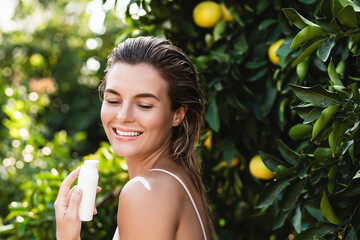 Sticker - Joyful and beautiful woman applying moisturizing cream or sunblock on her body