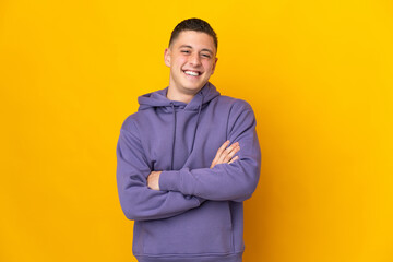 Young caucasian man isolated on yellow background keeping the arms crossed in frontal position