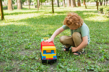 Wall Mural - full length view of redhead boy playing with toy truck on green lawn.