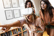 © BalanceFormCreative - Female friends use virtual reality devices at home. They are laughing and having fun.
