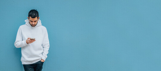 fashionable young man with mobile phone on blue street wall