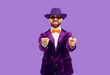Portrait of excited male entertainer in velvet suit isolated on purple studio background point at screen. Smiling disco man or performer show at camera make choice. Choose you hand gesture.