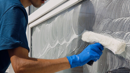 Wall Mural - Male professional cleaning service worker in overalls cleans the windows and shop windows of a store with special equipment