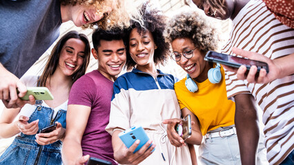 Diverse teenage students using digital smart mobile phones on college campus - Group of friends watching cellphones sharing content on social media platform - Youth, friendship and technology concept	