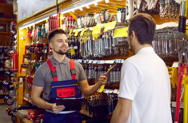 Wall Mural - Sales assistant at hardware store helping customer choose tools for home repairs. Salesman with clipboard offering good quality wrench to man who has come to DIY store to buy tools for his garage