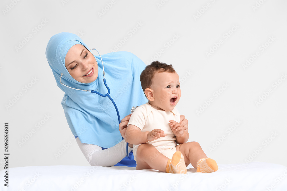Muslim pediatrician examining baby boy on light background
