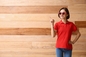 Wall Mural - Beautiful young woman in stylish polo shirt pointing at something on wooden background