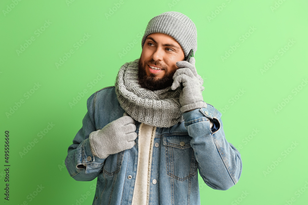 Handsome man in winter clothes talking by phone on color background