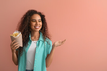 Canvas Print - Young African-American woman with french fries on color background