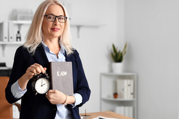 Wall Mural - Mature female judge with alarm clock and law book in courtroom