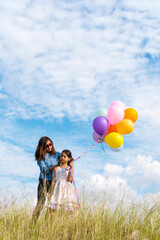 Wall Mural - Cheerful cute girl holding balloons running on green meadow white cloud and blue sky with happiness. Hands holding vibrant air balloons play on birthday party happy times summer on sunlight outdoor