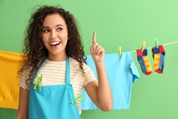 Wall Mural - Young African-American woman with hanging laundry and clothespins pointing at something on green background