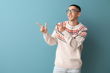 Wall Mural - Handsome young Asian man in knitted sweater pointing at something on blue background