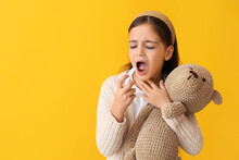 Little girl with toy using spray for sore throat on yellow background