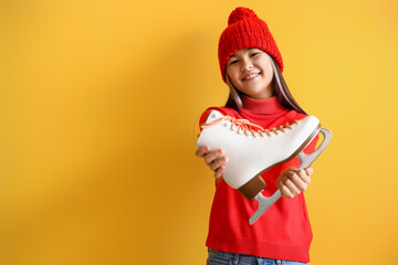 Poster - Little Asian girl in warm clothes with ice skate on yellow background