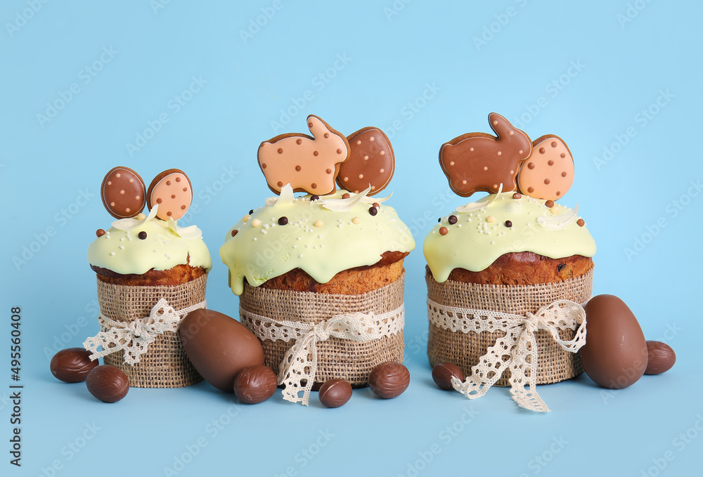 Delicious Easter cakes decorated with cookies and chocolate eggs on blue background