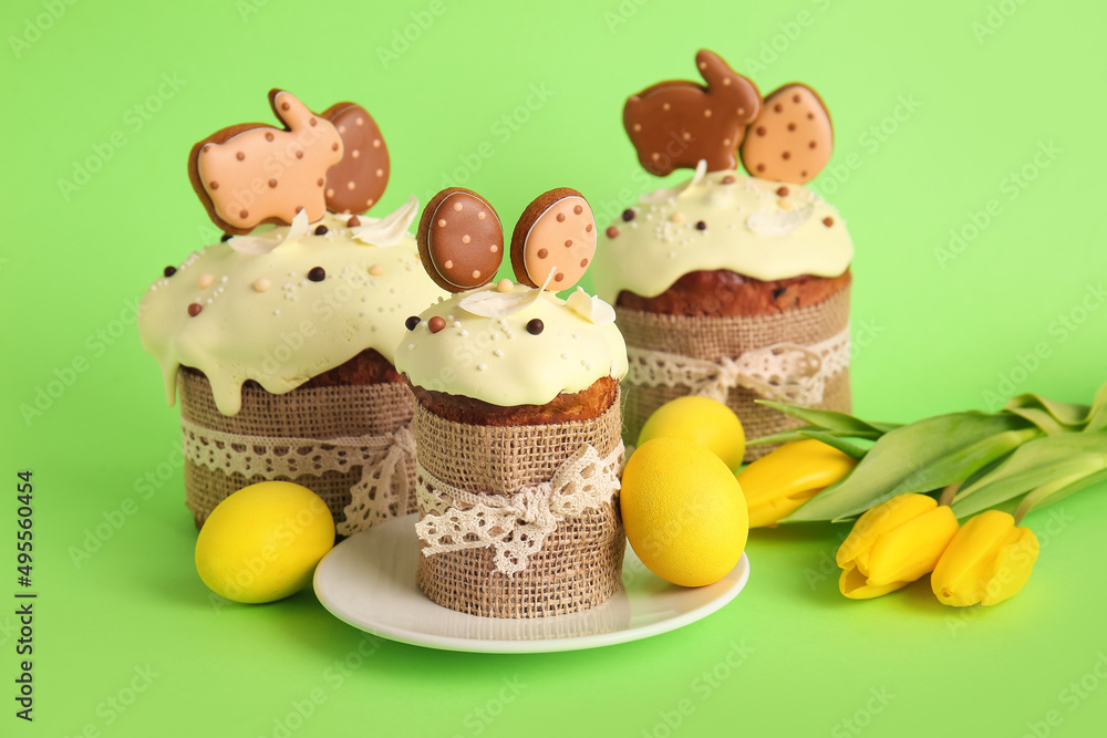 Delicious Easter cakes decorated with cookies, flowers and painted eggs on green background