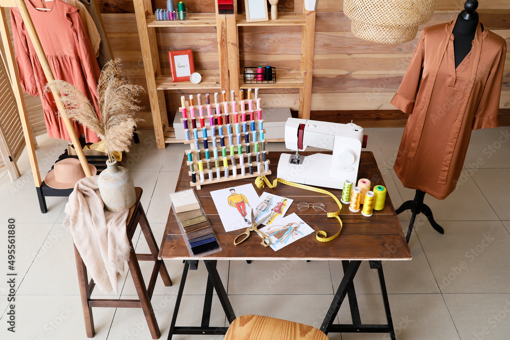 Tailor's workplace with sewing machine, thread spools and sketches in atelier