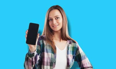 Wall Mural - Smiling beautiful woman wearing T-shirt against blue background  Hold mobile phone with blank empty screen