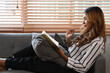 © Prathankarnpap - Pleased millennial woman reading book on couch at home.