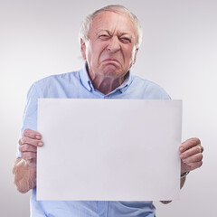 Who are you calling a grumpy old man. Studio shot of a senior man holding a blank sign and looking unhappy against a grey background.