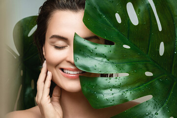 Wall Mural - young woman with a smooth skin holding monstera deliciosa plant leaf