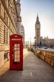 Fototapeta Big Ben - A classic, red telephone booth in front of the Big Ben clocktower in London, Westminster, during golden sunrise without people