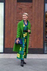 Full length portrait of fashionable aged woman in long green coat and elegant dress. Fashion Trend For Fall or Spring. Stylish Woman outfit with blue accessories