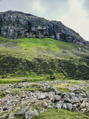 Sticker - Vertical shot of stones, grass and mountain peak against gray cloudy sky during daytime