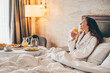 © Mariia Korneeva - Woman eating breakfast in the hotel room. Room service breakfast in hotel room.