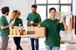 © Syda Productions - charity, donation and volunteering concept - happy smiling female volunteer with food in box pointing finger to herself and international group of people at distribution or refugee assistance center