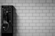 Black and white shot of a payphone a brick wall background