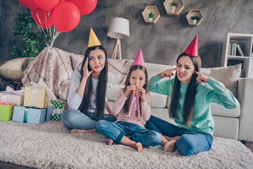 Canvas Print - Portrait of attractive annoyed family sitting on floor blowing festal whistle covering ears fooling at home indoors