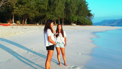 Sticker - Girls calmly relax on a beach with fine white sand bordered by a turquoise sea.Gili Meno, Indonesia