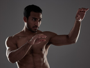 Wall Mural - Working on my fists of fury. Shot of a young man practicing his punches against a studio background.