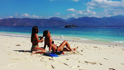 Sticker - Girls calmly relax on a beach with fine white sand bordered by a turquoise sea.Gili Meno, Indonesia