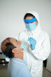 © DragonImages - Nurse in protective suit taking nasal swab from senior patient to test for possible coronavirus infection