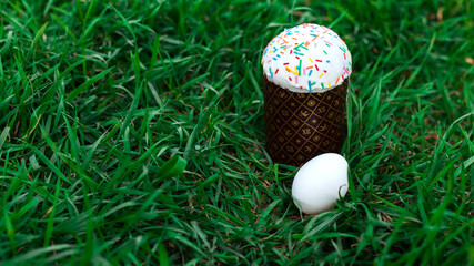 Easter cake with natural white eggs on green spring grass. Christian holiday in april or may season. Traditional orthodox russian or ukranian kulich with icing sugar. Side view, place for text, banner