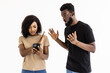 © F8  \ Suport Ukraine - Portrait of a serious young african man talking on mobile phone and showing silence gesture to his angry girlfriend over gray background