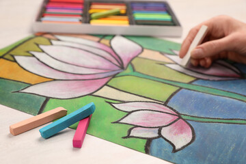 Wall Mural - Woman drawing beautiful lotus flowers on paper with soft pastels at white table, closeup