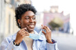 © ADDICTIVE STOCK - Cheerful black woman putting on medical mask