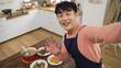 © PR Image Factory - mobile cam view of happy asian dad swave hand say hi to family through video chat online call at home. he looks at camera while smelling food and boasting about his cooking