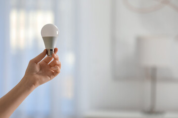 Woman holding fluorescent light bulb on blurred background, closeup with space for text. Saving energy concept